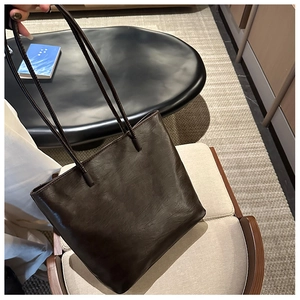 Detail view of dark brown tote bag with wrinkled leather texture and slim round handles