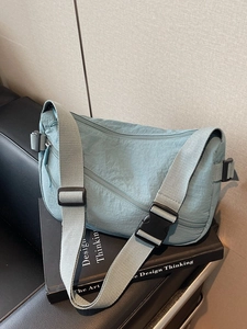 Minimalist mint blue nylon crossbody dumpling bag with wide adjustable shoulder strap on books