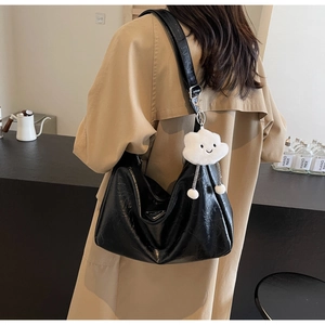 Detail shot of black wrinkled patent leather tote bag with cloud plush charm and metal badge