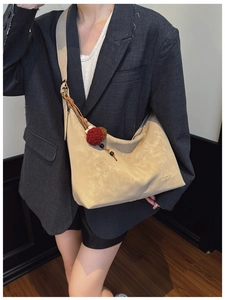 Detail of beige suede hobo bag featuring Merfil embossed logo and decorative pompom charm