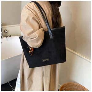 Detail of black suede tote bag with wooden bead charm and logo plaque shown on shoulder