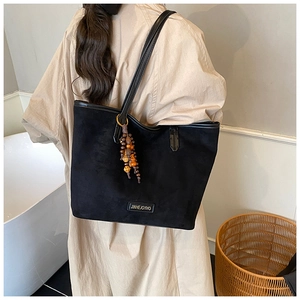 Detail of black tote bag featuring a colorful wooden bead tassel and metal brand logo