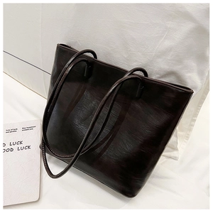 Detail of dark coffee leather tote bag showing glossy wrinkled texture and shoulder straps