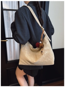 Detail of beige suede tote bag showing soft texture and MERFIL logo with ethnic charm