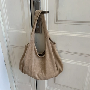 Detail of light brown suede hobo bag with wide strap hanging on a white wooden door