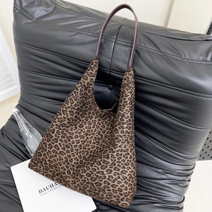 Détail du sac fourre-tout léopard avec lanières mauves sur un canapé en cuir noir