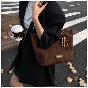 Detail of dark brown matte tote bag with unique beaded tassel charm on shoulder strap