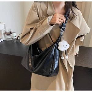 Detail of black pleated glossy shoulder bag with a plush cloud-shaped keychain charm