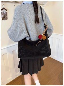 Detail of black frosted suede hobo bag with red pompom charm and PERFIL logo stamp