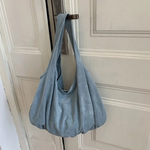 Detail view of large sky blue suede hobo bag hanging on a white door handle