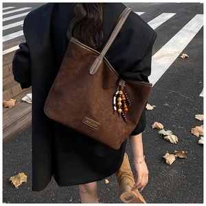 Detail of vintage brown suede tote bag with wood bead pendant and metal logo on street