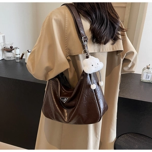 Detail of coffee brown pleated leather shoulder bag with plush cloud charm on a model