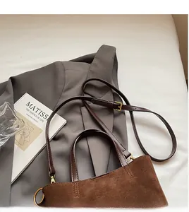 Detailed view of brown suede handbag featuring smooth leather straps and gold hardware