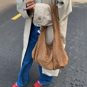 Lifestyle shot of a large brown suede tote bag styled with a trench coat and jeans