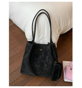 Detail of a black suede tote bag with golden logo and small accessory in a cozy setting