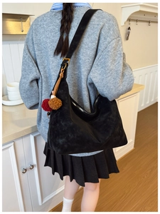 Close-up of matte black hobo bag with silver zipper and brown plush charm on shoulder strap