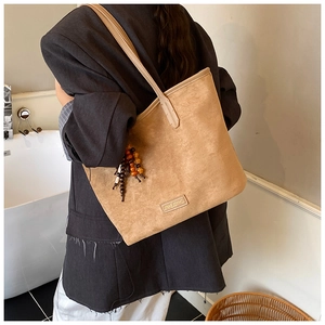 Detail of a brown suede tote bag featuring a vintage wooden bead pendant and logo plate