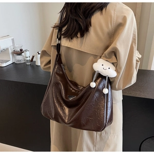 Detail of dark brown tote bag with glossy pleated leather and cloud plush charm