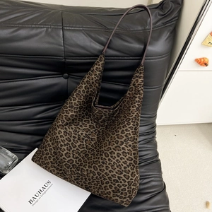 Détail d'un grand sac cabas en daim imprimé léopard posé sur un canapé en cuir noir