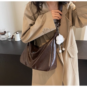 Detail of dark brown pleated leather shoulder bag with metallic logo and plush charm