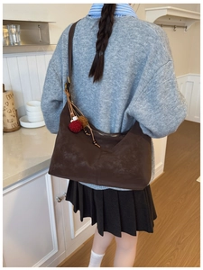 Detail of dark brown matte suede shoulder bag featuring plush charms and embossed logo