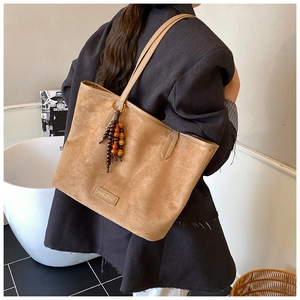 Detail of vintage brown suede tote bag with beaded tassel and metallic brand logo