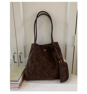 Detail of dark brown tote bag with matte texture, gold logo, and matching zippered pouch