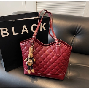 Detail of red quilted tote bag on leather sofa with a cute plush rabbit charm