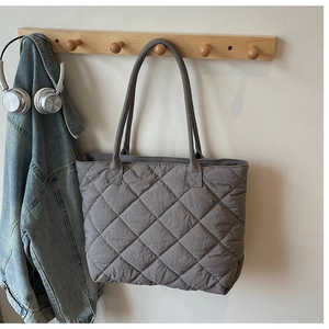 Détail du sac cabas gris matelassé avec surpiqûres losanges sur un support en bois