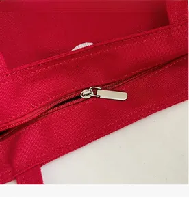 Close-up of a smooth silver metal zipper and neat stitching on a red canvas tote bag