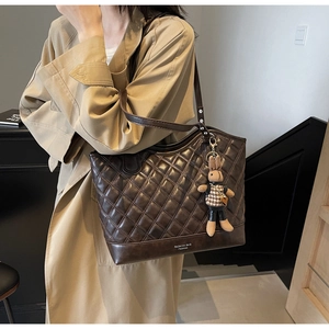 Detail view of large brown quilted tote bag with a cute plush rabbit pendant charm