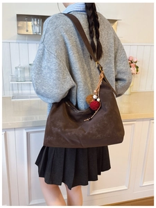 Detail of dark brown matte leather hobo bag with adjustable strap and ethnic tassel charm