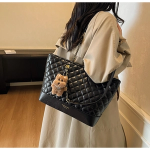 Détail du sac cabas matelassé noir avec logo doré et pendentif ours en peluche