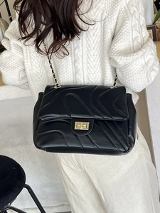 Black quilted crossbody bag with gold chain strap worn over a white cable knit sweater