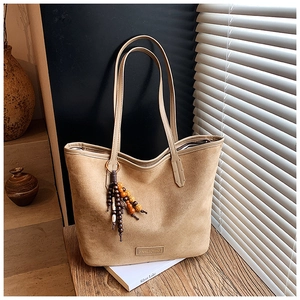 Detail of camel suede tote bag with wooden bead charm on a rustic wooden bench