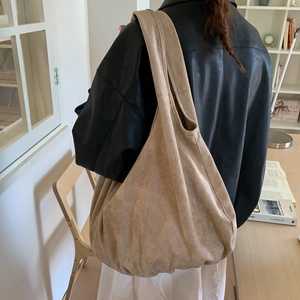 Detailed view of a large beige suede hobo bag styled with a black leather jacket