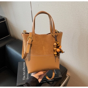 Detail of caramel suede and leather bucket bag with wooden bead charm and logo