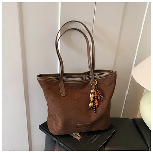 Close-up of brown suede tote bag with retro charm pendant and striped inner lining