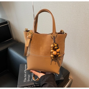 Détail du sac seau marron avec textures en daim mat et décoration de breloque en bois