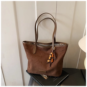 Detail of dark brown suede tote bag with vintage wood bead charm and brand plaque