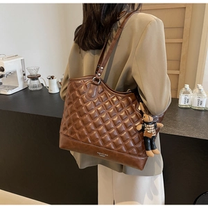 Detail of a dark brown quilted tote bag with a rabbit charm in a cozy cafe setting