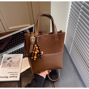 Détail du sac seau en daim marron mat avec pompon perlé et logo embossé sur le cuir