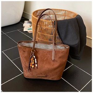 Close-up of brown suede tote bag with metal logo, beaded charm, and striped lining detail