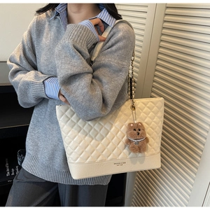 Détail du sac cabas beige matelassé avec chaîne dorée et breloque ours sur le mannequin