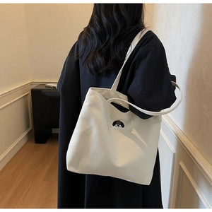 Detail shot of white canvas tote bag with dog embroidery worn by model in black coat