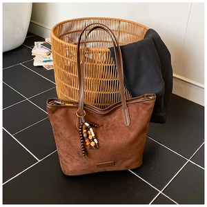 Detail of dark brown suede tote bag featuring metallic zipper and bohemian beaded charm