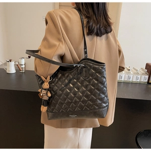 Detail of black quilted tote bag with a small rabbit charm shown on model's shoulder