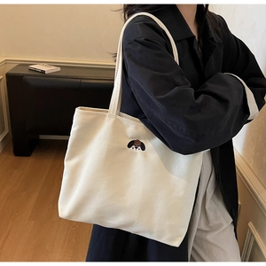 Detail of cute puppy embroidery on cream canvas tote bag worn by a model in casual setting