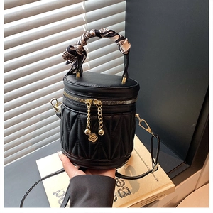 Detailaufnahme einer schwarzen gesteppten Zylindertasche mit goldenen Zippern und Seidenschal