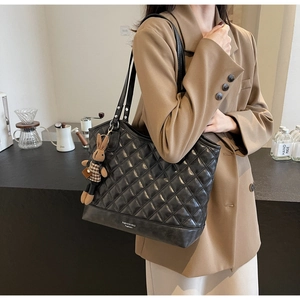 Detail of black quilted bucket bag with long shoulder straps and rabbit charm
